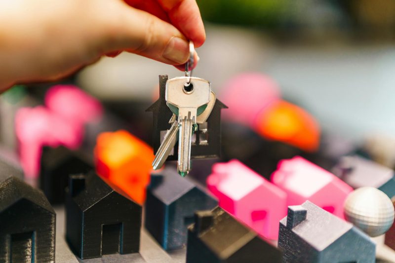 Colorful miniature houses and a hand holding keys representi 1776186179
