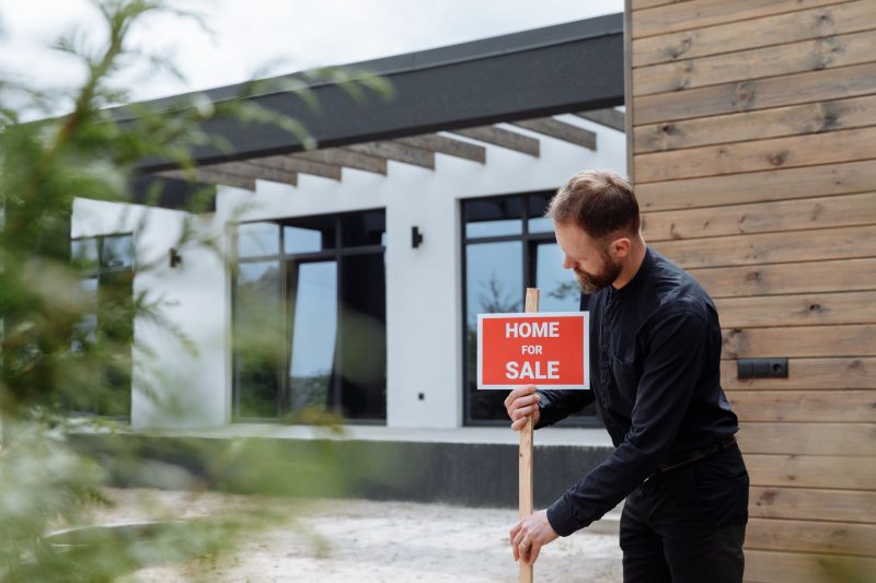 Home 24 Man placing a home for sale sign outside a modern house for 1785862952