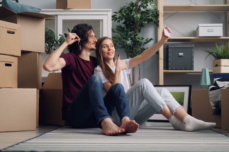 Home 23 Young couple sitting among moving boxes taking a selfie cele 1791306358